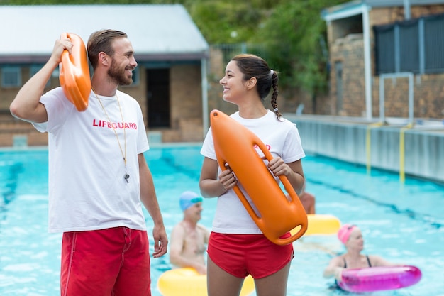 Salva-vidas masculinos e femininos segurando latas de resgate à beira da piscina