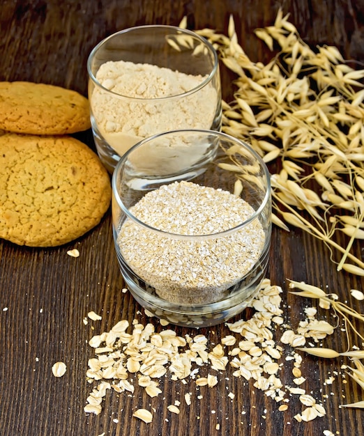 Salvado pequeño y harina de avena en dos vasos de avena y galletas de orejas sobre un fondo de tablas de madera