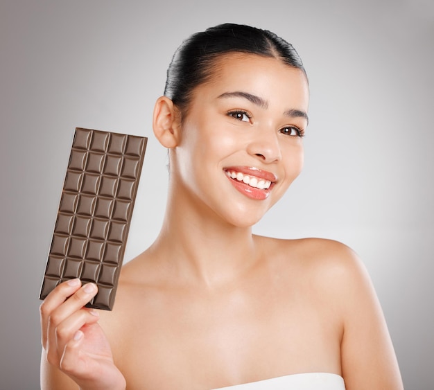 Salve a Terra, é o único planeta com chocolate Foto de estúdio de uma jovem atraente comendo um pedaço de chocolate contra um fundo cinza