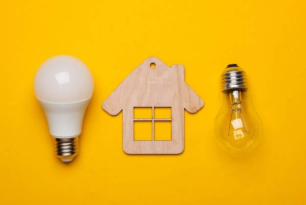 Salve o conceito de energia. Conceito de casa ecológica. Mini casa, lâmpada incandescente e economizadora de energia em fundo amarelo