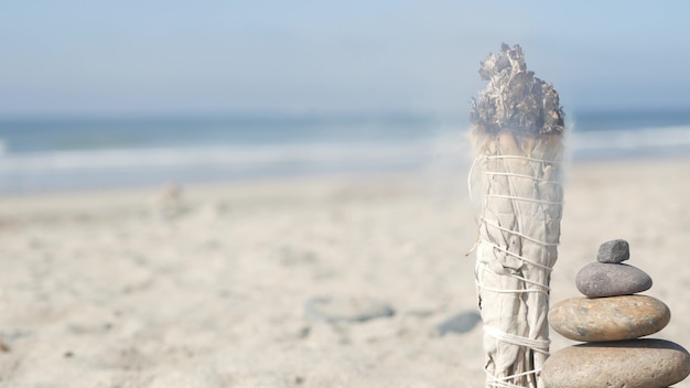 Salvia blanca seca, mancha ardiendo, aroma manchado. Equilibrio de rocas en la playa del océano, piedras de cantos rodados