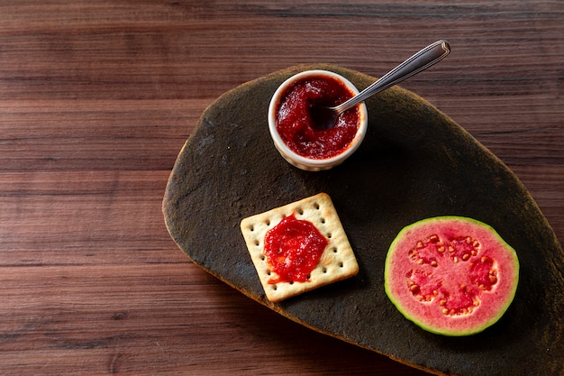 Salz- und Wassercracker, Schüssel mit Guavenmarmelade und Guavenscheibe auf rustikalem Stein