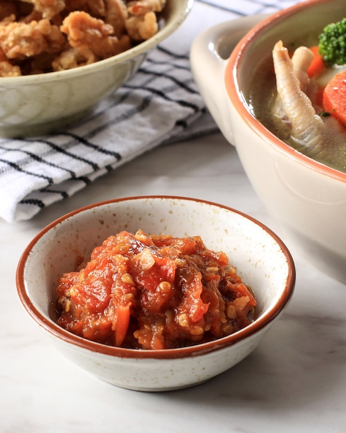 Sambal Terasi, traditionelle indonesische Chilisauce mit Garnelenpaste, Tomaten und Chili, Beilage für das Tagesmenü. Serviert auf kleiner Schüssel, weißer Tisch