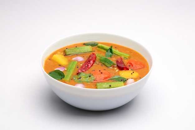 Sambar, caril vegetariano misto organizado em uma tigela branca sobre um fundo branco texturizado.