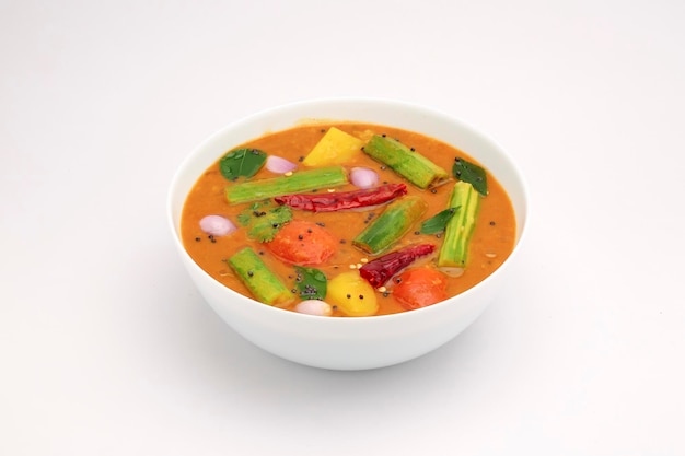 Sambar, curry vegetariano mixto dispuesto en un tazón blanco sobre un fondo blanco texturizado.