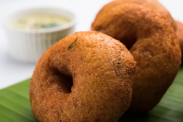 Sambar vada ou Medu Vada, uma comida popular do sul da Índia servida com chutney de verde, vermelho e de coco sobre um fundo sombrio. Foco seletivo