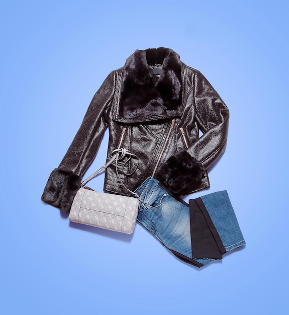 Sammlung von Damenbekleidung auf blauem Hintergrund. Komposition mit Lederjacke, Jeans und Handtasche