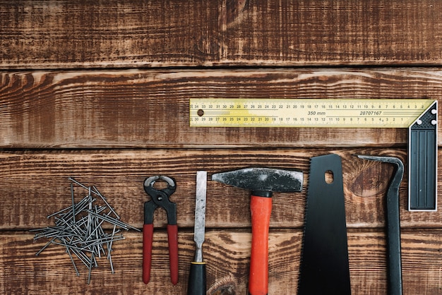 Sammlung von Holzbearbeitungswerkzeugen auf einem Holztisch und Kopierraum: Zimmerei, Handwerkskunst und handgefertigtes Konzept, flache Lage. Säge, Hammer, Meißel, Nägel, Lineal.