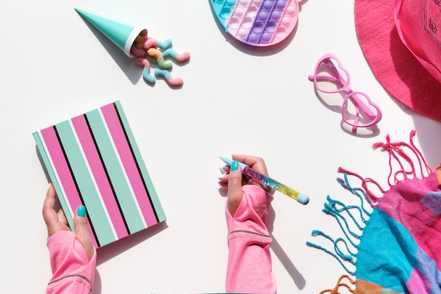 Sammlung von Party-Objekten und Süßigkeiten auf geometrischem Papier flach legen Pralinen-Notizbuch und Regenbogenstift in der Hand Geometrischer geschichteter Hintergrund in kräftigem Pink und Mintblau auf Weiß