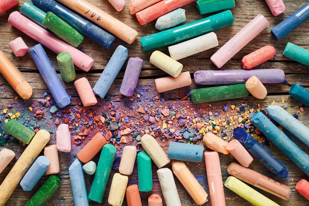 Sammlung von regenbogenfarbenen Pastellstiften mit Pigmentstaub auf altem Schreibtisch