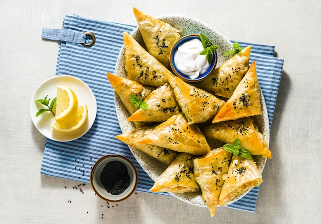 Samosa indiana feita com massa folhada com batata picante e vegetais, servida com iogurte, hortelã e limão em guardanapo azul em restaurante