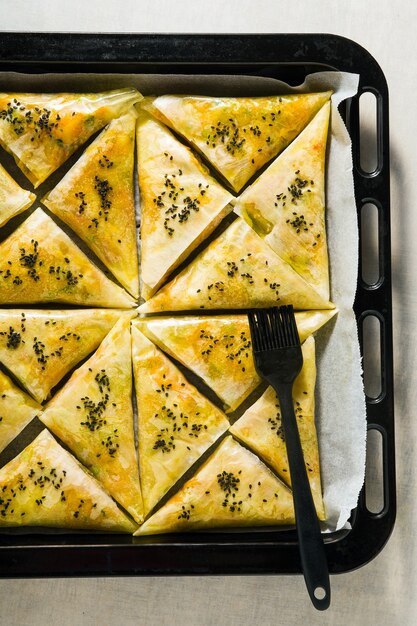 Samosa indiana feita de massa folhada com batata picante e legumes em uma assadeira, pronta para ser assada no forno com sementes de gergelim preto