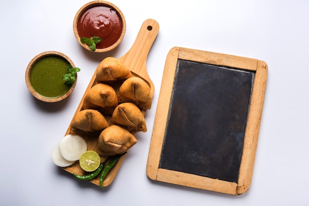 Samosa-Snack serviert mit Tafel oder Schiefertafel für Text, serviert mit Ketchup und Minz-Chutney