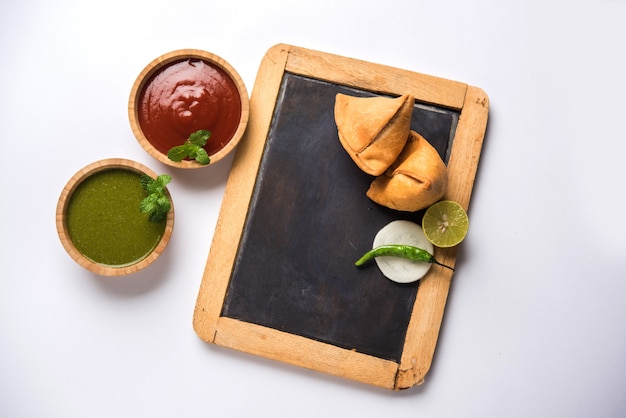 Samosa-Snack serviert mit Tafel oder Schiefertafel für Text, serviert mit Ketchup und Minz-Chutney