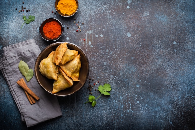 Samosas indias: pasteles fritos / horneados con relleno sabroso, bocadillos indios populares, servidos en un tazón con especias y cilantro fresco sobre fondo rústico, vista superior. Sobrecarga de samosas con espacio de copia