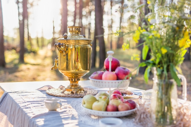 Samovar ruso con tazas sobre una mesa con manzanas y ramo de flores de campo