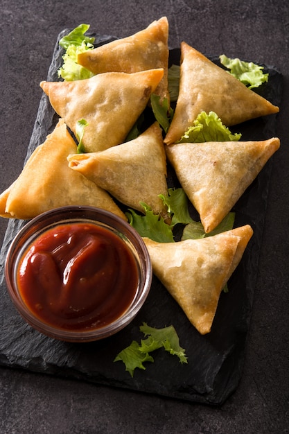 Samsa o samosas con carne y verduras sobre fondo negro. comida tradicional india.