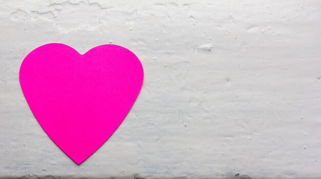 San Valentín - colores magenta de corazón de papel contra la superficie pintada de blanco