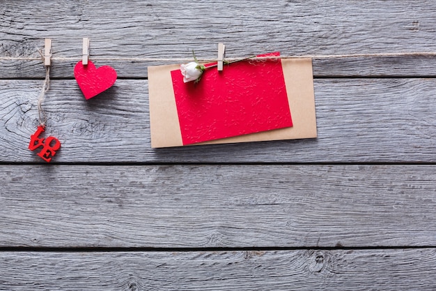 Foto san valentín con corazón de papel rojo y tarjeta de felicitación vacía en pinzas para la ropa en tablones de madera rústica