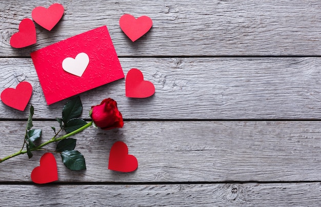 San Valentín con flor rosa roja, corazones de papel hecho a mano y tarjeta en madera rústica