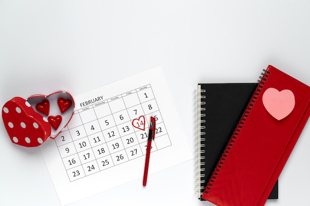 Foto san valentín en la oficina. caja de bombones en forma de corazón, calendario de febrero y cuadernos sobre una mesa blanca.