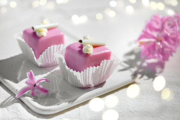San Valentín petit fours con glaseado de mazapán. Flor de jacinto rosa fragante. Guirnalda de luces sobre textil blanco. ¡Feliz día de San Valentín! Velada romántica en casa.
