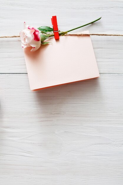 San Valentín, tarjeta de felicitación vacía y flor color de rosa en pinza para la ropa en tablones de madera rústica blanca