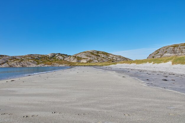 Sand an einem leeren Strand mit blauem Himmel kopieren Raum Schöne Landschaft einer malerischen Meeresküste mit felsigen Bergen oder Hügeln am Horizont an einem klaren Sommertag mit Copyspace