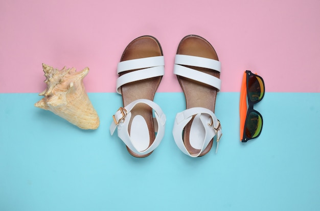 Sandalias de cuero de moda para mujer, conchas marinas, gafas de sol sobre una superficie de color pastel, vista superior, endecha plana