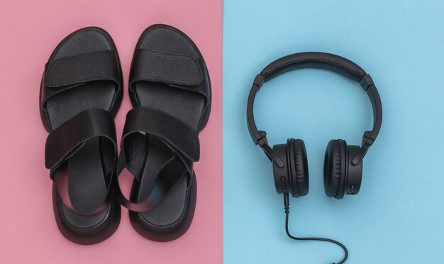 Sandalias de cuero negro y auriculares estéreo sobre fondo rosa pastel azul. Vista superior