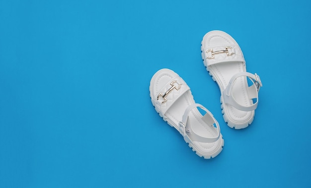 Sandálias de couro branco feminino em um fundo azul Conceito mínimo de sapatos femininos de verão