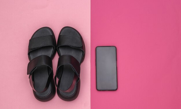 Sandalias de mujer de cuero negro y smartphone sobre fondo rosa. Vista superior. Endecha plana