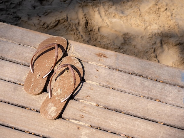 Las sandalias de mujer manchadas de arena vacías se quitaron en la terraza de madera y se fueron a caminar por la playa al atardecer con espacio para copiar Vacaciones de verano viajes de fin de semana al mar conceptos