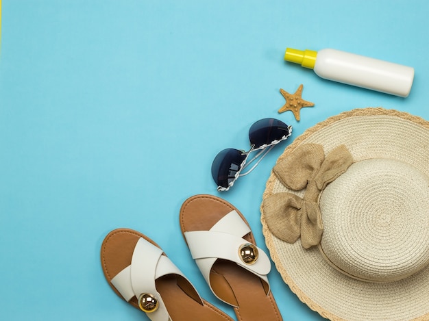 Sandalias de mujer, sombrero, bolso y protector solar sobre un fondo azul. Espacio para el texto. Concepto de vacaciones. Endecha plana.