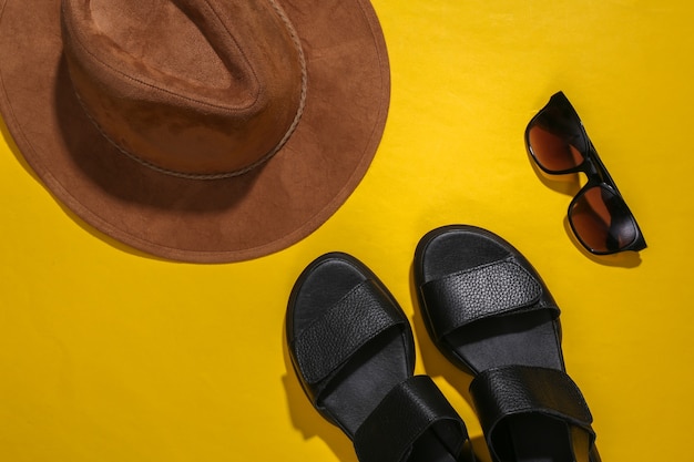 Sandalias de mujer, sombrero y gafas de sol sobre un fondo amarillo. Complementos de mujer. Vista superior