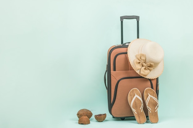 Sandalias de mujer, un sombrero y una maleta con asa sobre fondo azul. Espacio para el texto.