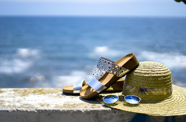 Sandalias de mujer, sombrero de paja y gafas de sol con el mar de fondo