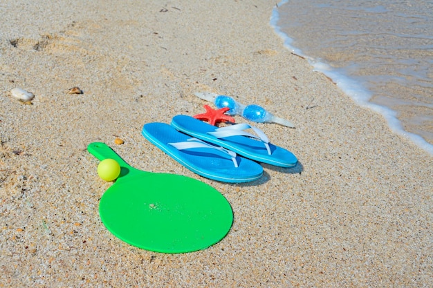 Sandalias, raquetas y gafas de mar en una orilla dorada.