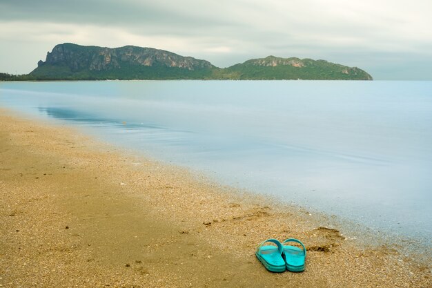 Foto sandalias rosas en la playa con la montaña en el mar son fondo