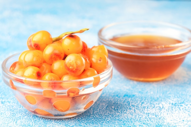 Foto sanddornbeeren in der schüssel und im natürlichen honig oder im sanddornöl auf blauem hintergrund