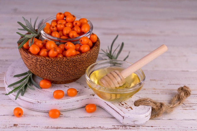 Sanddornbeeren und -honig auf einem weißen hölzernen hintergrund. Gesundes Ernährungskonzept.