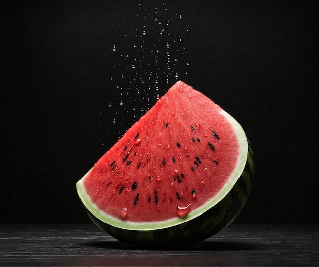 Sandía con gotas de agua en una mesa de madera con fondo negro