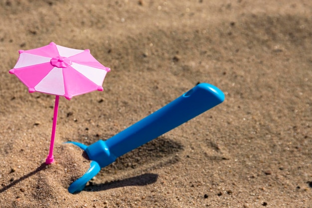 Sandkasten für Kinder ein Spielzeug rosa Regenschirm und eine blaue Schaufel an einem Sandstrand Urlaub mit Kindern Psychedelika für Kinder