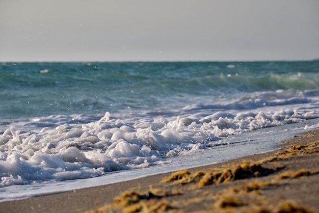 Sandstrand am Meer mit schäumenden Wellen, die an der Küste zermalmen