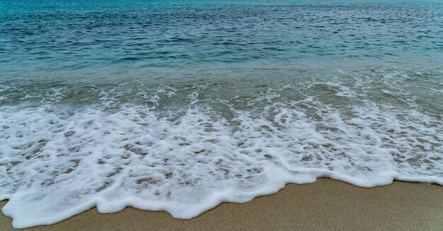 Sandstrand am Meer mit weißem Schaum und Welle vom blauen Meer