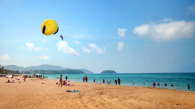 Sandstrand, Fallschirmspringen über dem Meer an einem sonnigen Tag, leichte Wolken am blauen Himmel Parasailing