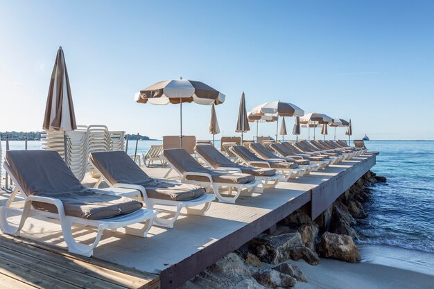 Sandstrand mit leeren sonnenliegen am pier an einem sonnigen tag im resort. französische riviera. tourismus und reisen.