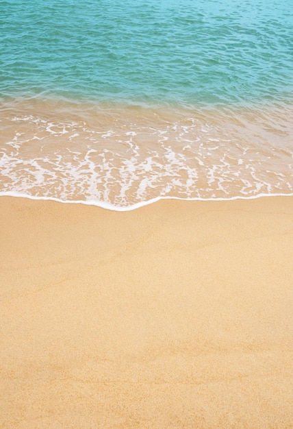 Sandstrand und blaues Meer mit sanfter Wellenform auf Sandstruktur. Braune Strandsanddüne an sonnigen Frühlingstagen. Vertikale Draufsicht für den Hintergrund des Sommerbanners