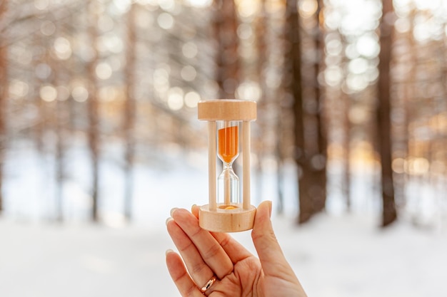 Sanduhr als Symbol für den Wechsel der Jahreszeiten Schneeschmelze Sanduhr in der Hand einer Frau im Winter