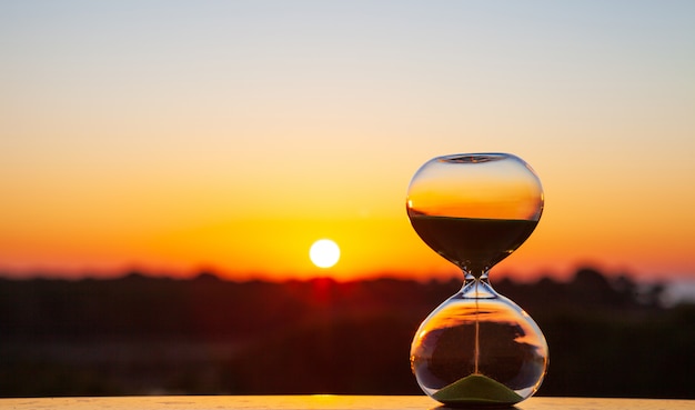 Sanduhr bei Sonnenuntergang oder Morgengrauen auf einem verschwommenen Hintergrund, als Erinnerung an die verstrichene Zeit